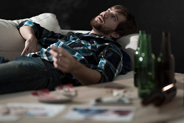 Stoned man lying on couch with beer bottles on table Young handsome stoned man lying on a couch substance intoxication stock pictures, royalty-free photos & images