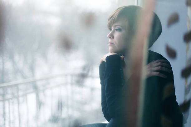 sad girl on the windowsill looking out the window