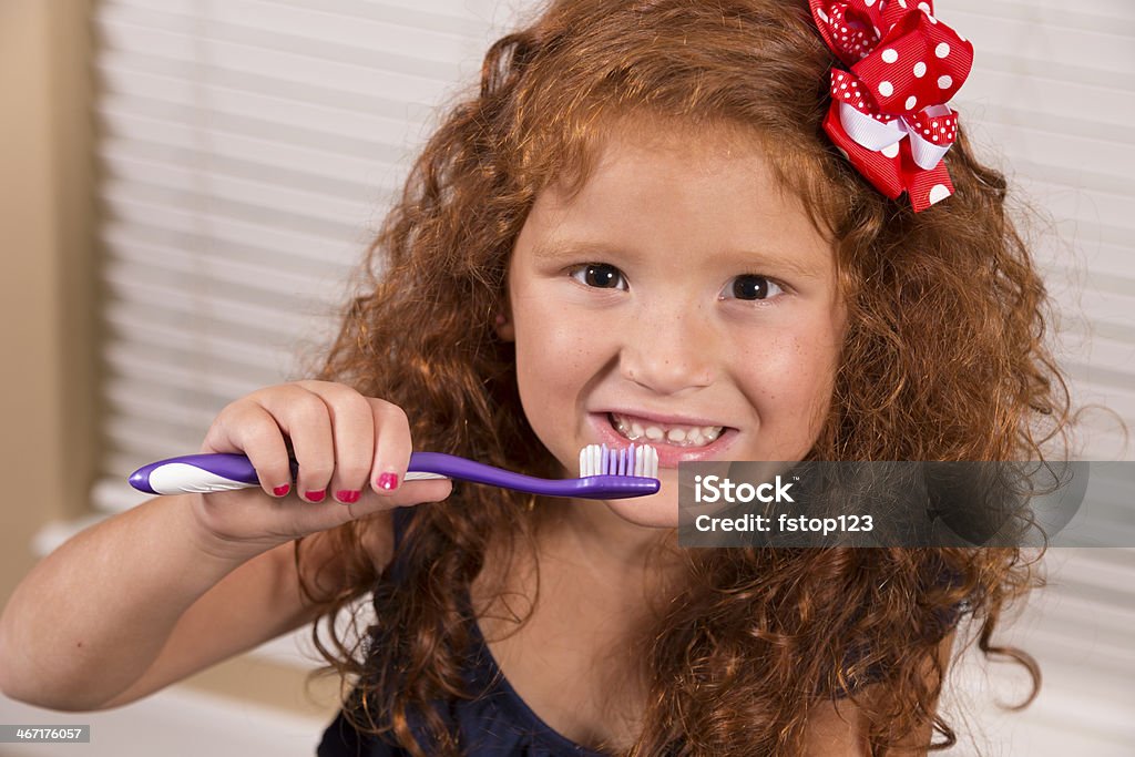 Healthy Lifestyle:  Happy young red-haired girl brushing her teeth. Happy, elementary-age girl brushing her teeth. Beautiful child with long red curly hair.    4-5 Years Stock Photo