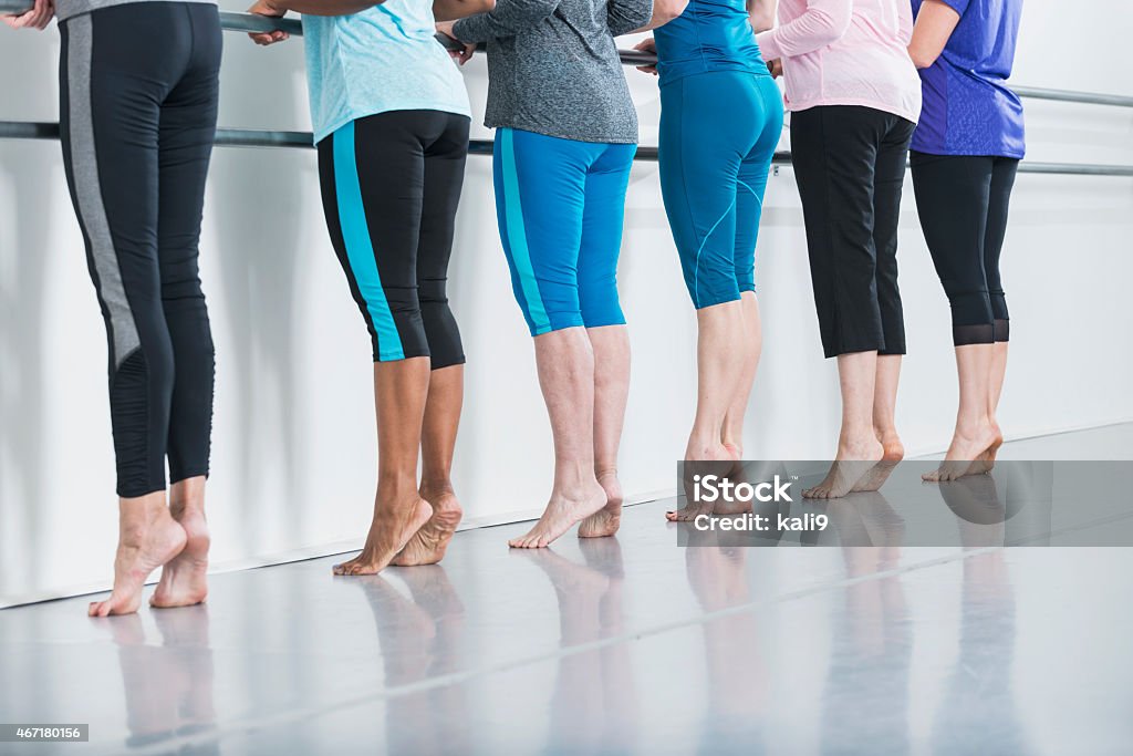 Exercise class A cropped rear view of a group of six women in a dance studio taking a barre fitness class.  They are unrecognizable, visible only from the chest down.  They are standing in a row on the balls of their feet, against the wall holding the barre. Barre Stock Photo