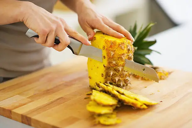 Photo of closeup on woman cutting pineapple