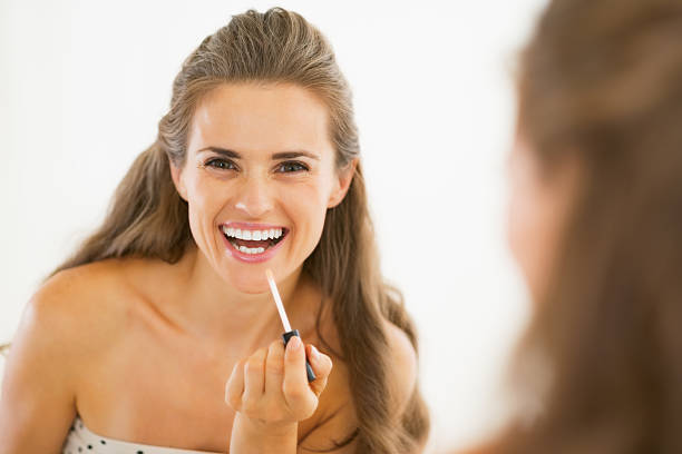 istock happy young woman applying lip gloss in bathroom 467198285