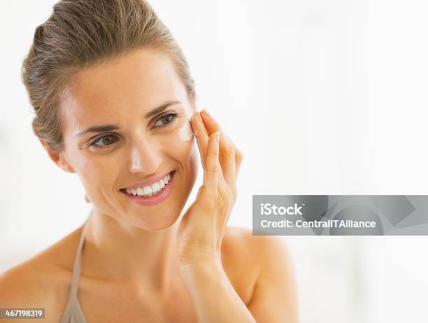 Portrait Of Happy Young Woman Applying Cream In Bathroom Stock Photo - Download Image Now