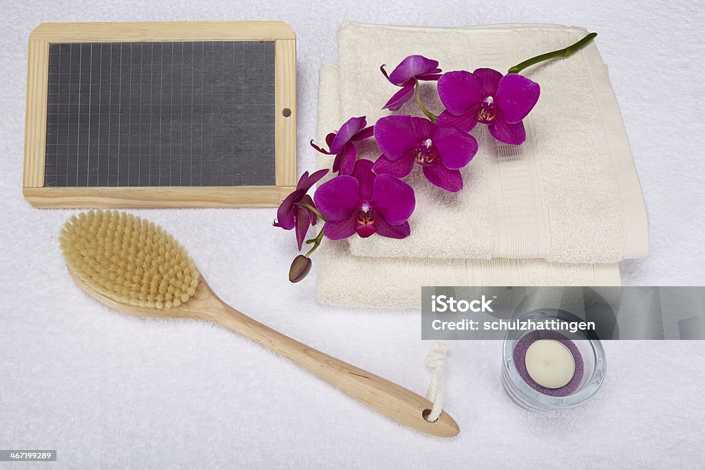 Wellness - Bath brush, towels and decoration with slate A bath brush is laying beneath two folded, naturally colored towels. A slate can be used as a free text area. The scene is decorated with a purple orchid and a tealight into a glass bowl. Back Brush Stock Photo