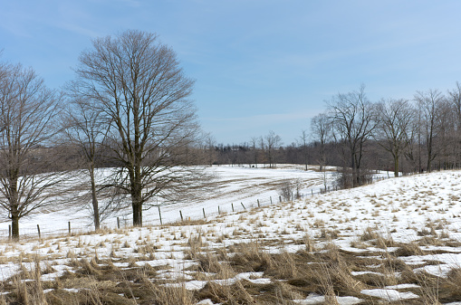 A view of rural rolling farm fields on a late winter day. Signs of spring are evident as the snow melts away, creating an abstract pattern of snow and dormant grass in the hay field.