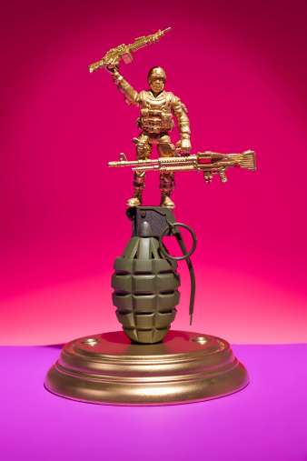 A marine figurine stands ontop of a grenade on a trophy base against a colorful background.