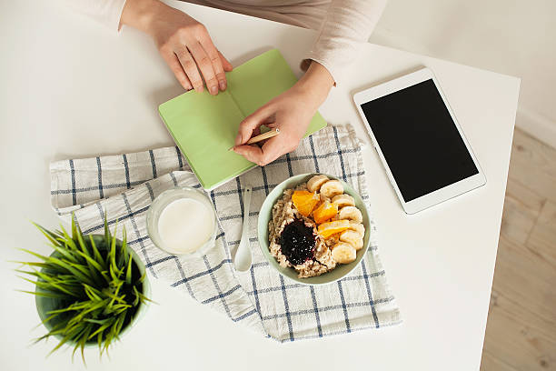 Woman making notes in notepad with healthy food on table stock photo