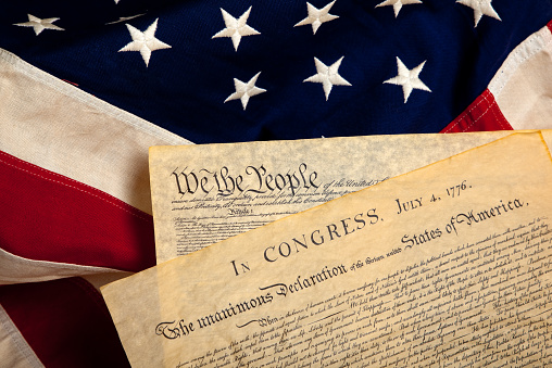 United States' Constitution and Declaration of Independence on a flag background