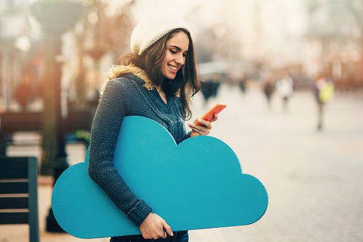 Woman with  a big blue cloud on the street, using a smart phone.