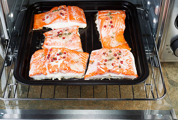 Freshly Baked Salmon in Oven Tray Horizontal photo of Baked Wild Red Salmon pieces coated with dried red peppercorns and sea salt inside oven with stone counter top underneath sockeye salmon filet stock pictures, royalty-free photos & images