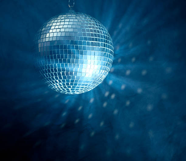Image of lit disco ball hanging over a darkened dance floor stock photo