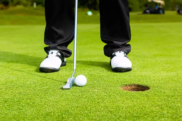 Golf player putting ball into hole, only feet and iron to be seen