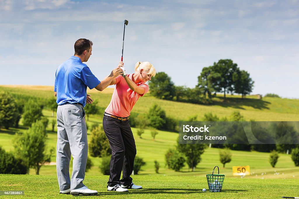 Young female golf player on course Young female golf player at Driving Range with a Golf Pro, she presumably does exercise Golf Stock Photo