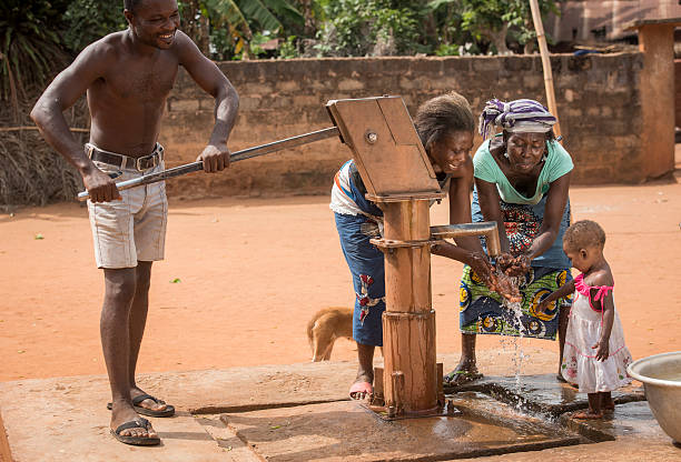 African family at a well Village de Guede Codji, Benin, March 09, 2015: Grandmother, mother, father and small child at a well. The man is pumping water, while his family is washing their hands and haveing a refreshiment. This well provides clean water for the whole village. benin stock pictures, royalty-free photos & images