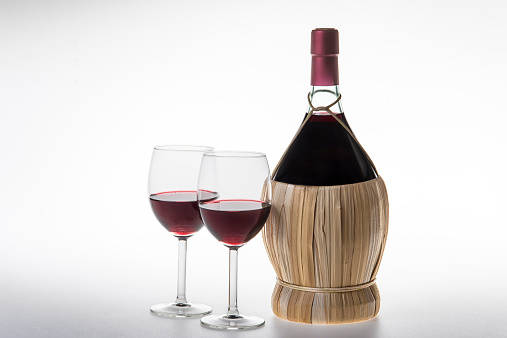 Chianti Bottle, fiasco, and two glasses of red wine on white background