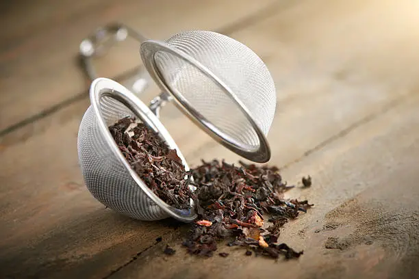 tea ball with black tea and red fruit close up in a tea restrainer on a wooden table