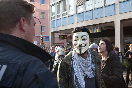 Frankfurt, Germany - March 18, 2015: Protestors at Blockupy 2015 demonstration during inauguration of European Central Bank in the city center of Frankfurt. A young man with a Guy Fawkes mask talks to a police officer. Blockupy is a left-wing political network of several organizations. The name derives from its plan for a \