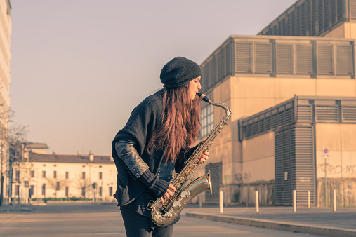 Beautiful young woman playing tenor saxophone in the city streets