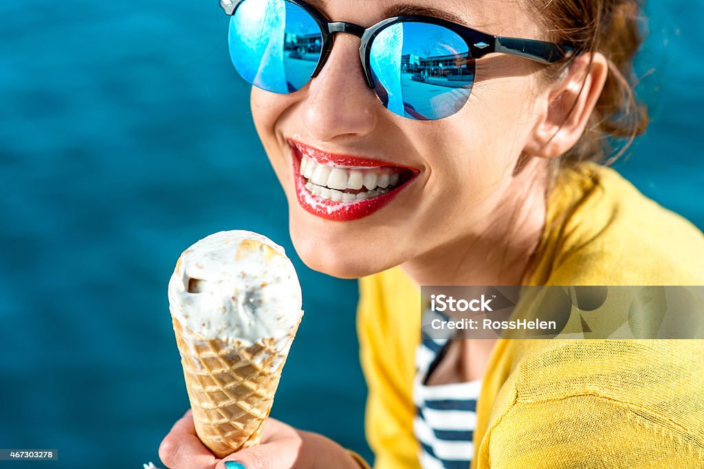 Woman with ice cream Young woman in yellow sweater and sunglasses eating ice cream on the blue water background Eating Stock Photo