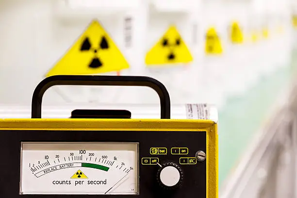 Photo of Geiger counter with yellow hazard signs in row fading behind