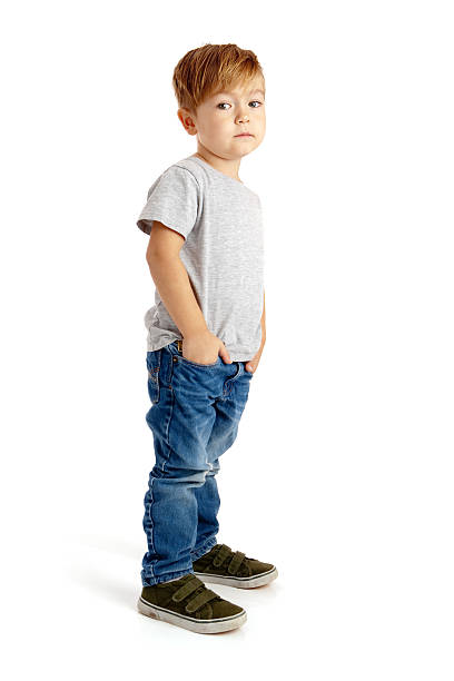 Little Boy on White Background with Hands in Pockets Preschool boy standing on white background wearing jeans and t-shirt, with hands in pockets and sad expression. sad child standing stock pictures, royalty-free photos & images