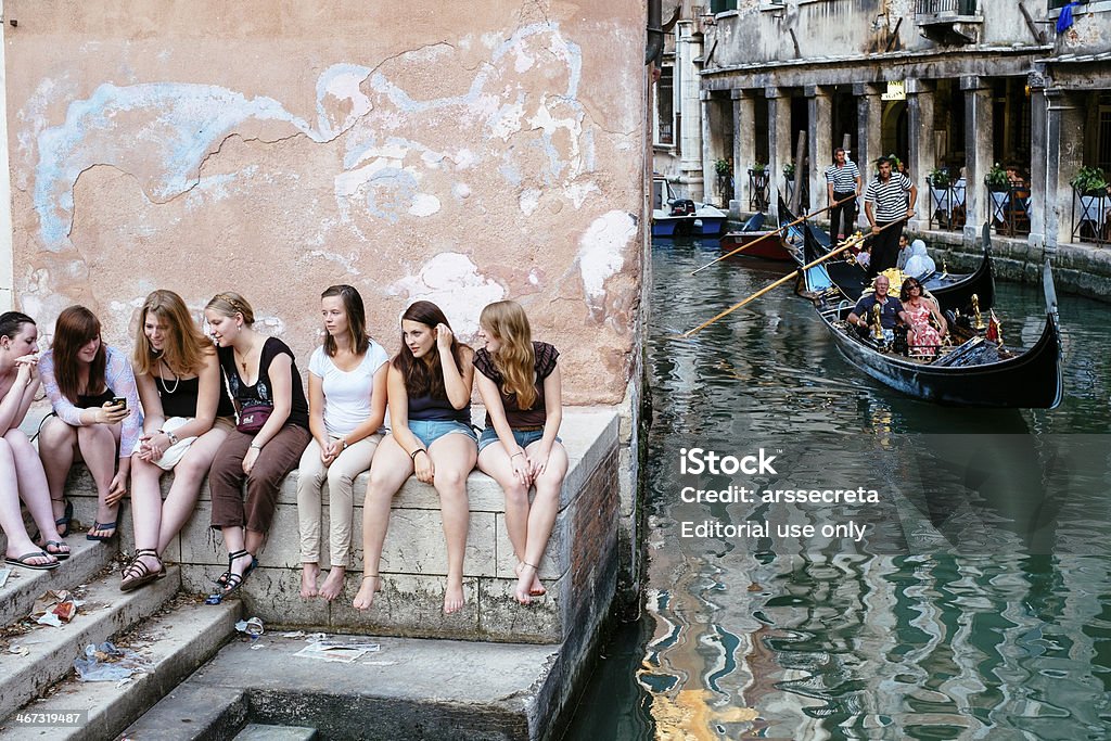 Girls at small canal Venice, Italy - July 18, 2012: A group of young girls take a rest near a small canal, with a gondola passing by. Canal Stock Photo