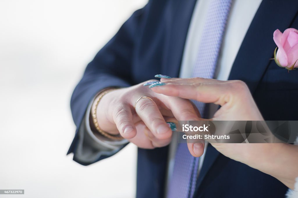 Bride wears ring to bridegroom's finger. Bride's POV Bride wears ring to bridegroom's finger. Bride's POV. Bridegroom dressed in a blue suit with pink flower in the front pocket of jacket, white shirt and dotted necktie. Photo was taken during the marriage ceremony. Bride is very accurate. 2015 Stock Photo
