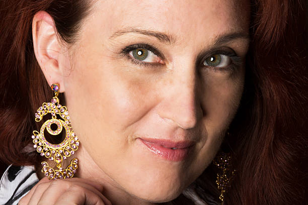 Closeup of smiling woman showing off earings. Horizontal full frame closeup studio shot of woman with central heterochromia wearing long sparkly earings. hazel blue eyes stock pictures, royalty-free photos & images