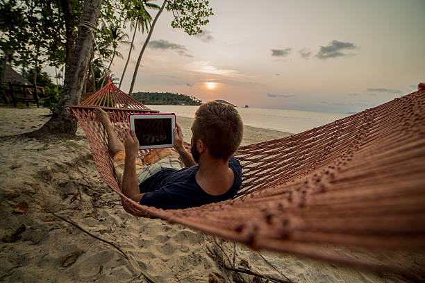 homme sur hamac relaxant-tablette numérique - reading beach e reader men photos et images de collection