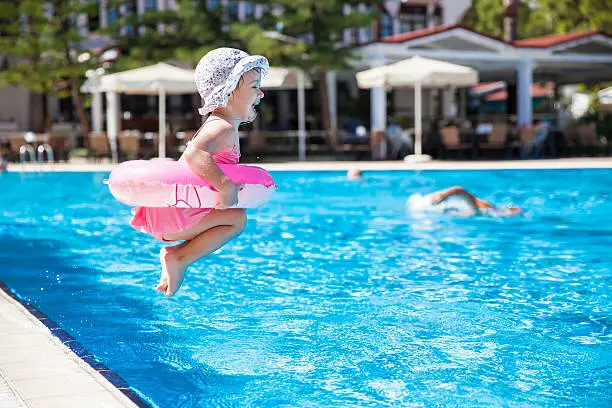 Photo of Toddler dressed in pink and jumping into a swimming pool