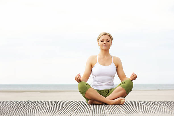 hermosa joven mujer sentada en postura de loto yoga en la playa - exercising female isolated relaxation fotografías e imágenes de stock