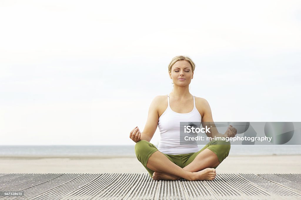 Beautiful young woman sitting in yoga lotus pose at beach Portrait of a beautiful young woman sitting in yoga lotus pose at the beach Yoga Stock Photo