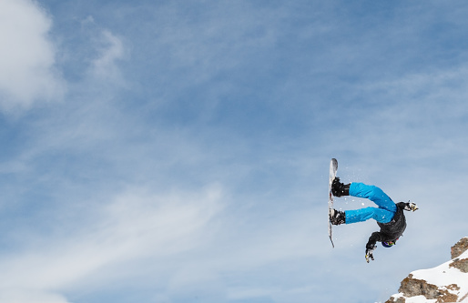 Snowboarder (boy, male) doing an acrobatic backflip after a jump.  With copyspace and blue sky.