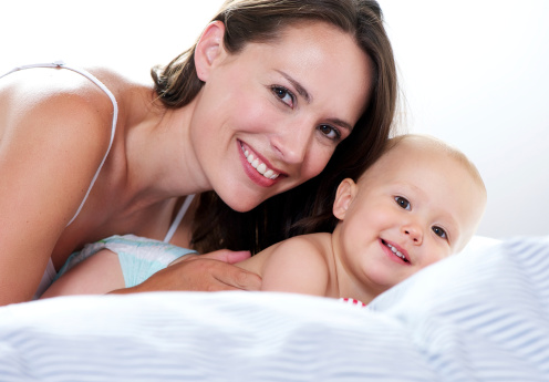 Close up portrait of a mother and baby smiling on bed
