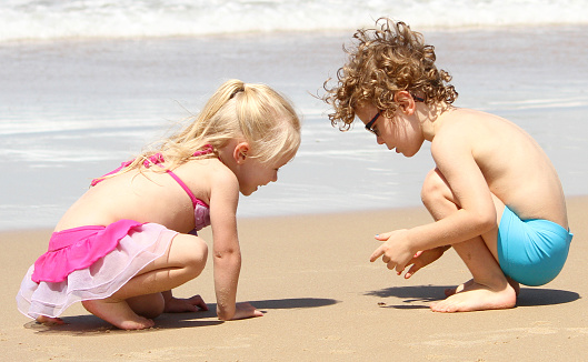 A little boy and girl, brother & sister, boy and girl look at crab on the beach, wearing swimmers, having fun.