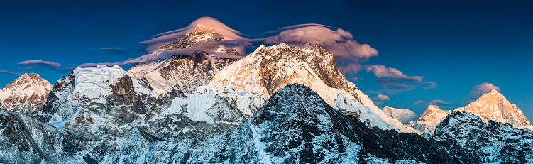 Lenticular clouds caressing the iconic pyramid peak of Mt. Everest (8848m) as delicate alpenglow light illuminates the south west face and the summits of Nuptse (7861m), Lhotse (8516m) and Makalu (8463m) in this vibrant Himalaya mountain panorama deep in the Sagarmatha National Park of Nepal, a UNESCO World Heritage Site. ProPhoto RGB profile for maximum color fidelity and gamut. 