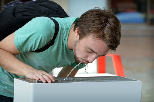 Close up of one young male wearing sunglasses drinking at a water fountain