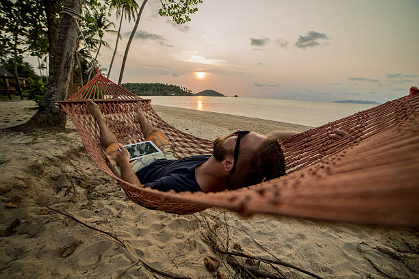 istock Young man on hammock at sunset with digital tablet 467346636