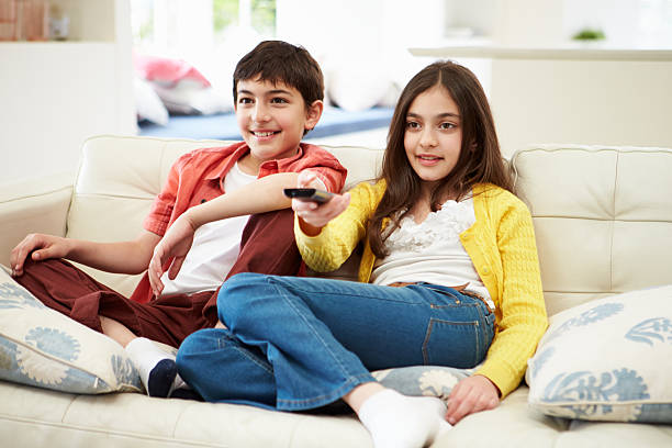 istock Two Hispanic Children Sitting On Sofa Watching TV Together 467348327