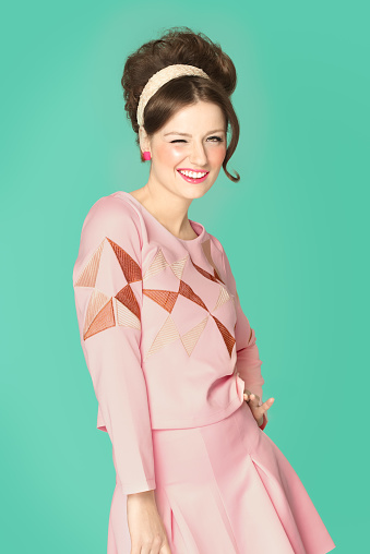 Woman in sixties style fashion posing with wink. Pink and cyan retro colors. Sixties hairstyle.