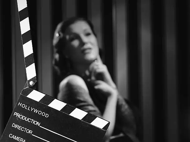 Hollywood black and white, a beautiful acting woman and a clapboard - minimal lighting and strong contrast