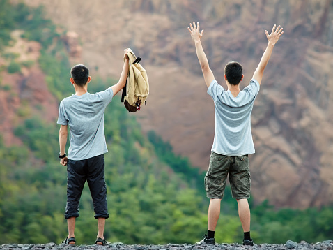 Two happy young tourist men standing on rocky cliff and enjoying nature