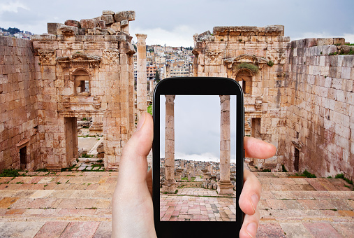 travel concept - tourist taking photo of ancient town Gerasa and modern city Jerash in Jordan on mobile gadget