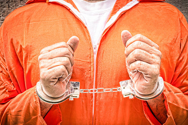 istock Handcuffed Hands - Guantanamo prison orange clothes 467357487