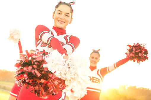 Group of cheerleaders performing outdoors  - Concept of cheerleading team sport training at high school during sunset - Tilted horizon composition and warm filter with sun backlighting