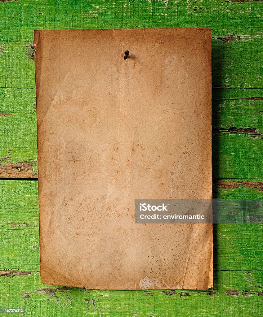 Antique paper blank notice hanging by a nail on wood. A very old vintage blank piece of paper as a notice for copy space hanging by a rusty nail pinning the paper on a green weathered wood board wall. The lighting is natural daylight coming from the left of the scene causing the texture and shadows to stand out. 2015 Stock Photo