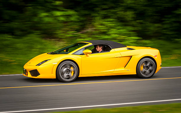Bright yellow Lamborghini Gallardo driving on road. Vancouver, Canada - June 8, 2013: A yellow Lamborghini Gallardo is seen being driven on the road by a young male driver, during a local "Cars and Coffee" event. street racing stock pictures, royalty-free photos & images