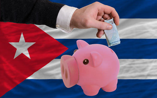 Man putting euro into piggy rich bank and national flag of cuba in foreign currency because of insecurity and inflation