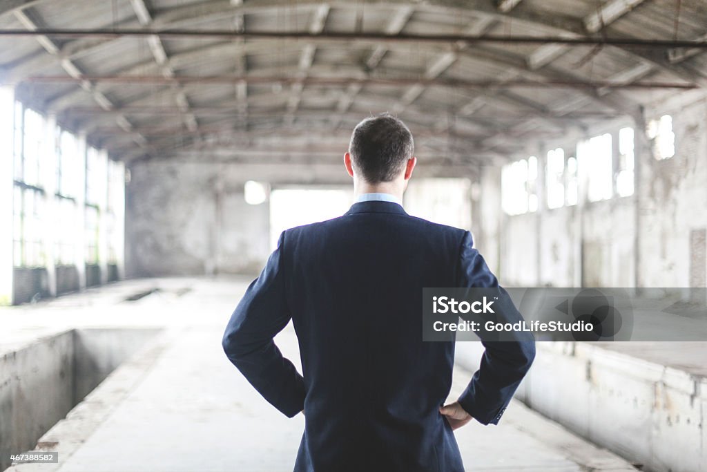 What to do? Unrecognizable businessman standing in a empty factory thinking. Rear view, adult Caucasian (investment or real estate concept) Investment Stock Photo