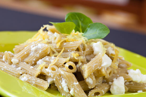 Very close view of plate with piccolini pasta garnished with ricotta cheese and lemon zest and decorated with valerian leaves.